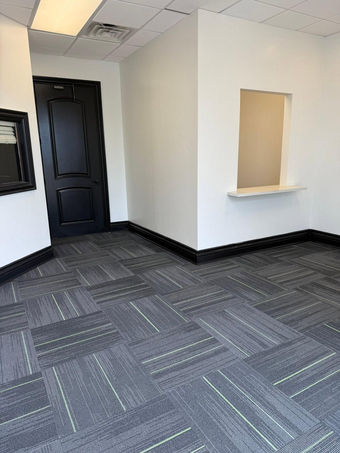 Completed Audibel Gretna office with painted walls, carpet tile, black door, and service window ledge